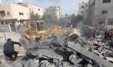 A bulldozer and a number of people can be seen in the rubble of a building attacked by Israel