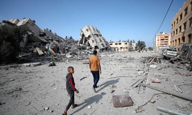 Two people are seen walking amid ruins of large apartment buildings
