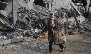 A woman with a shopping bag walks past a building that has been bombed in the Khan Younis area of Gaza 