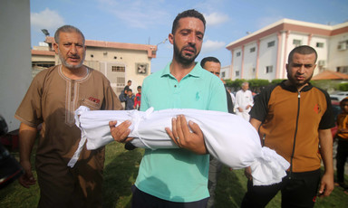 Man holds the body of a child wrapped in cloth 