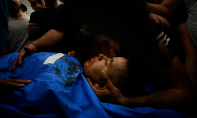 A boy lies on a stretcher as another boy embraces him 