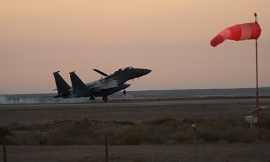 Warplane mid-air appears to be landing in an open field in a dimly lit sky 
