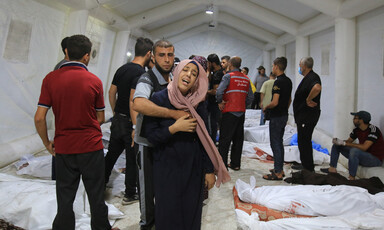 A man wraps his arm around a crying woman as they stand in a tent surrounded by shrouded bodies lying on the ground