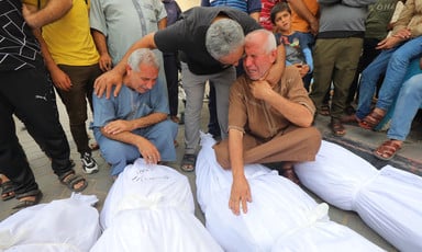 Men weep over bodies wrapped in white burial shroud 
