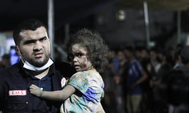 A medic wearing a face mask on his chin carries a child 