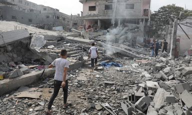 Young people walk on rubble in front of bombed-out residential building