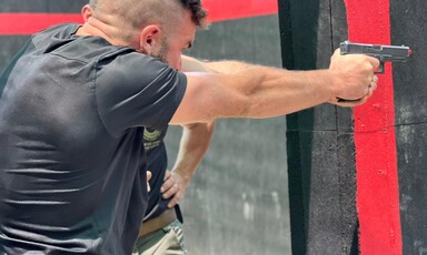 A man with a shaved head holds a gun and aims at a target 