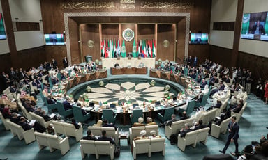 Desks are arranged in a circle in front of a number of flags at the Arab League headquarters in Cairo