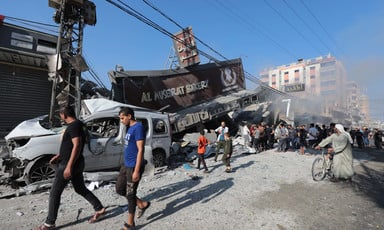 People walk past the wreckage of a bakery and a car