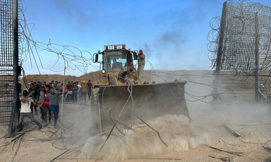 A bulldozer drives through a metal fence