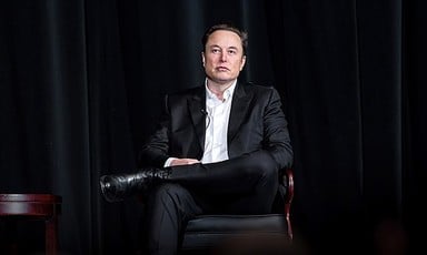 Elon Musk, CEO of X, sits on a chair wearing a dark suit and a white shirt 