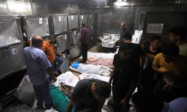 Men stand around bodies wrapped in makeshift shrouds lying on the ground