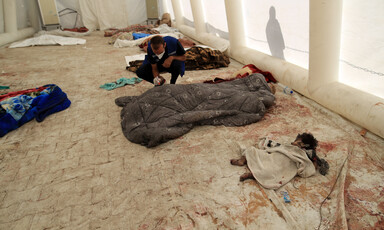 The partially covered body of a toddler lies net to the bodies of adults covered in blankets