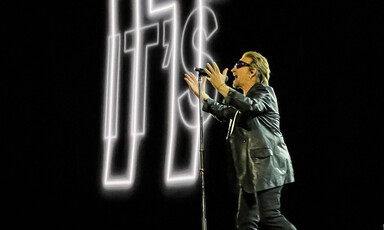 The rock star Bono wears shades as he holds a microphone stand