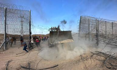 Excavator scoop moves through empty space in fence covered with barbed wire