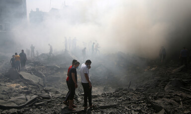 People shrouded in smoke walk through rubble