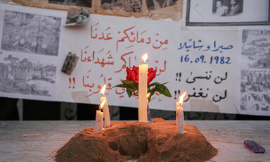 Three lit candles stand before posters remembering the massacres of Palestinian in Lebanon during Israel's invasion which started in 1978 