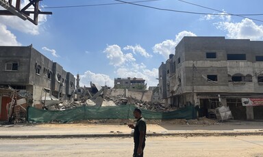 A man stands beside a building in Gaza that has been destroyed by Israel 