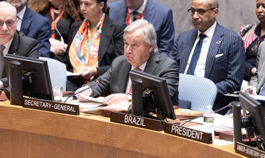 Antonio Guterres holds a piece of paper while sitting at a table with a microphone in front of him