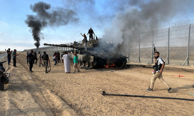 People climb on top of a burning Merkava tank as black smoke and flames rise from it