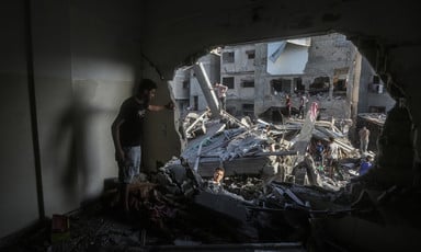 A man looks through a large hole in a building that has been attacked 