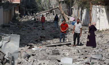 Two men walk down a street that is covered in gray rubble and debris