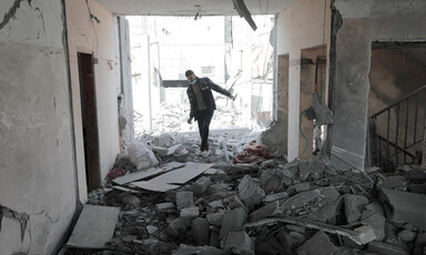 A man wearing a mask on his chin in the remains of a home following an Israeli airstrike in Gaza. 