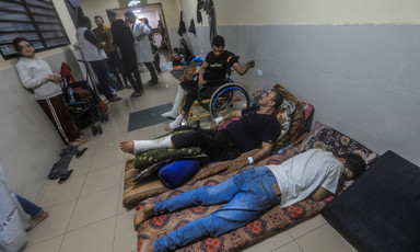 Two men lie on the ground beside a man in a wheelchair in a hospital corridor 