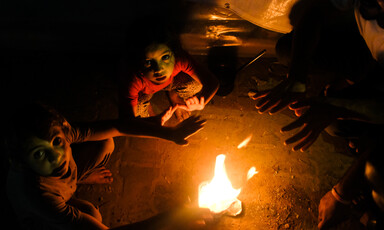 A man and two children warm themselves by a fire