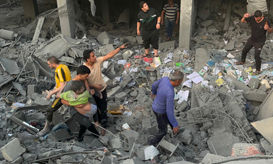 A child is carried by a young man amid the remains of a building that has been attacked in Gaza 