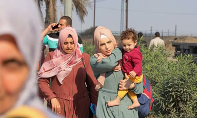 A woman carrying a child walks beside another woman as they flee from one part of Gaza to another. 