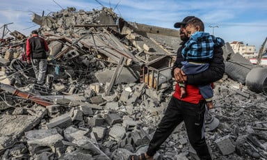 A man carries a child in what remains of a home 