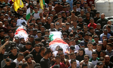 A massive crowd of people carries two bodies wrapped in flags 