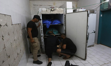 Men inspect a fridge with bodies in it at a morgue 