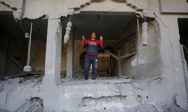 A young man wearing a dark blue tracksuit stands in what remains of a building 