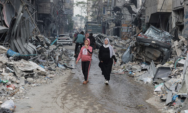 A woman and a girl walk through a devastated refugee camp in Gaza 