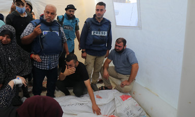 Wearing a flak jacket marked press Al Jazeera journalist Wael al-Dahdouh stands beside a number of other people with the dead bodies of his family members on the floor