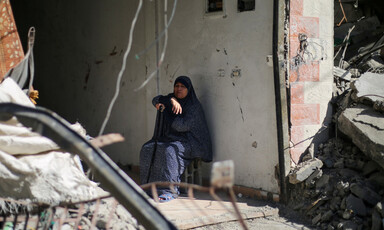 A woman sits by a wall surrounded by rubble