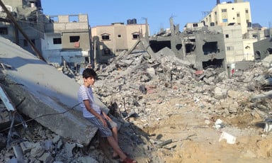 A boy sits looking at rubble