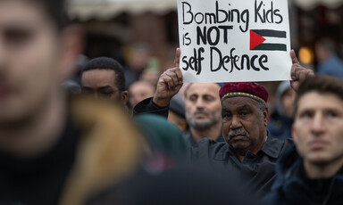 A man holds a sign reading bombing kids is not self defence