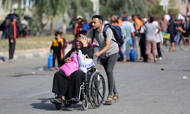 A man pushes a woman in a wheelchair with a group of people on foot behind them