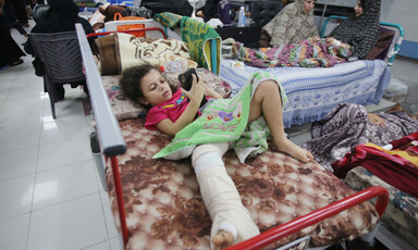 A girls plays on a phone in hospital bed, her leg in plaster