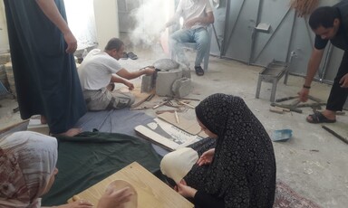 A woman shapes bread dough while a man bakes it atop an open-air oven