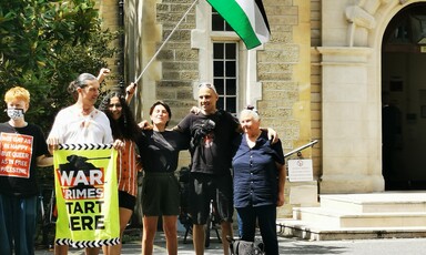 Some members of the campaign group Palestine Action hold a banner reading war crimes start hear and a Palestinian flag outside a London court