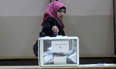 A woman casts a paper vote into a ballot box