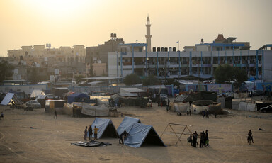 Landscape view of people standing next to several tents in front of school and sky with a yellow glow