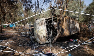 Burned out, overturned bus lies amid debris and trees