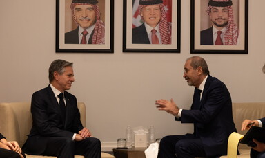 Two men in suits sit across from each other in reading chairs conversing 