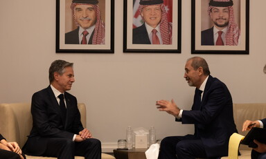 Two men in suits sit across from each other in reading chairs conversing