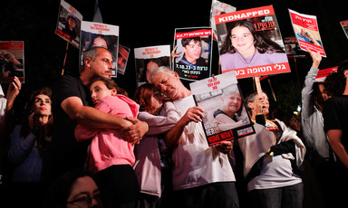A man hugs a young girl as people hold picket signs showing photos of captives in the outdoors at night